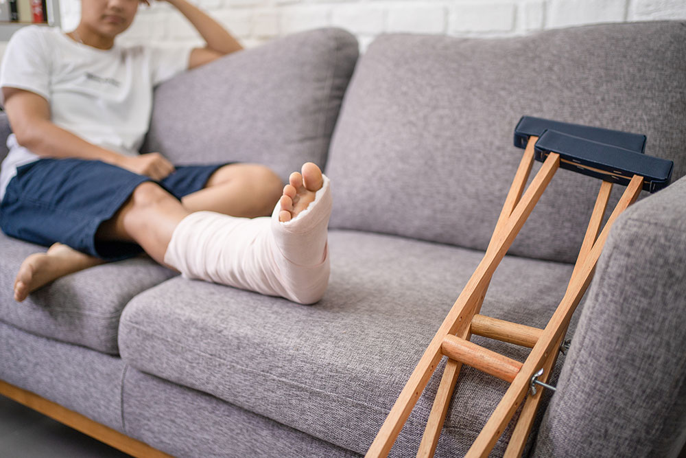 person sitting on a couch with leg in a cast and crutches near by